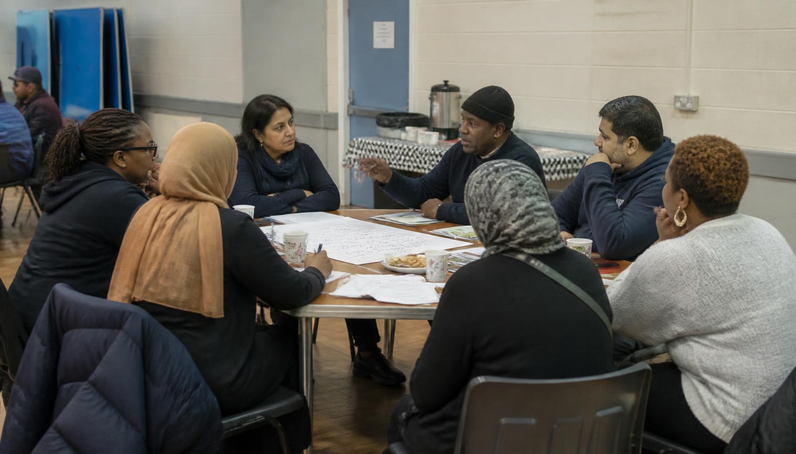 A diverse residents' group meeting around a table in a community hall